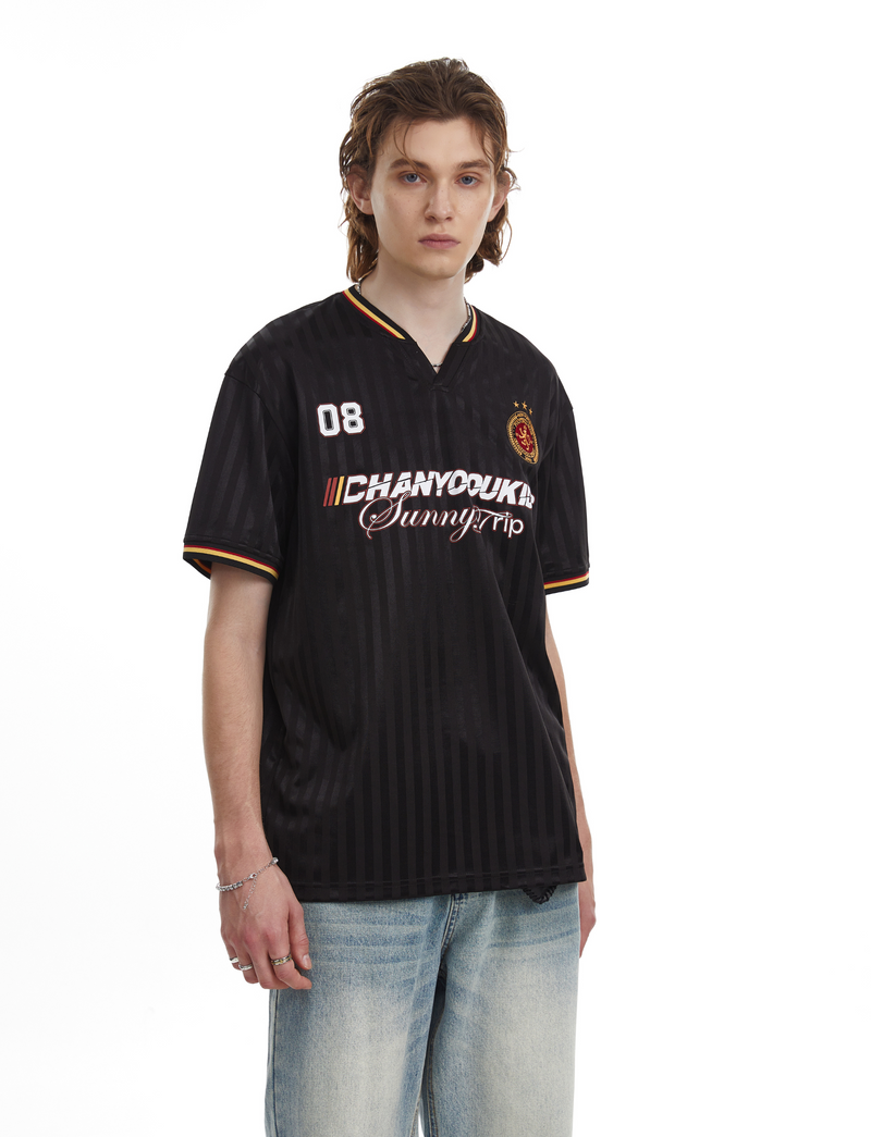 Black varsity-style mesh soccer jersey tee with striped trim, chest graphics, and relaxed fit on model