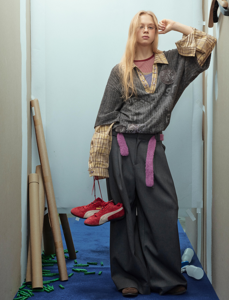 Model posing in black bear graphic sweater with plaid sleeves and wide gray pants
