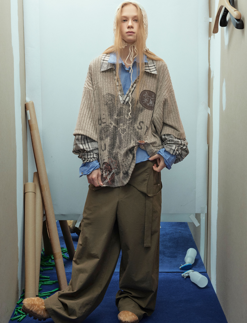 Model wearing beige bear graphic sweater front view with plaid sleeves and layered shirt hem