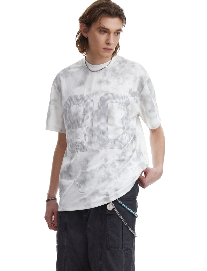 Model wearing a marble wash oversized tee with large 26 graphic, distressed details, and black cargo pants