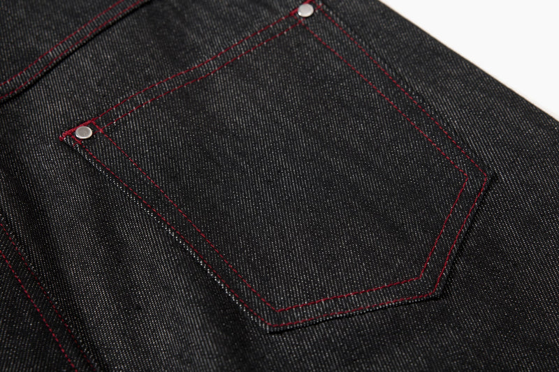 Close-up of black denim back pocket with red contrast stitching and rivet accents