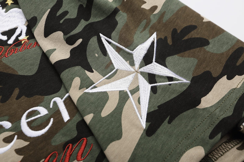 Close-up of a camo polo shirt with embroidered star and streetwear lettering in green, black, beige, and brown tones