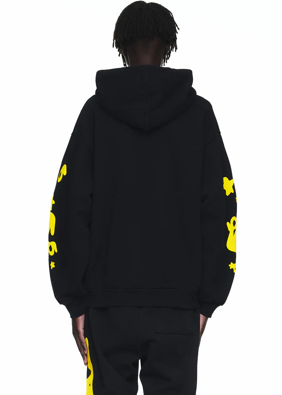 A person wears the Black Graphic Hoodie with Star Lettering Print, a comfort fit pullover featuring bright yellow sleeve graphics, paired with black pants. Shown from the back against a plain white background.