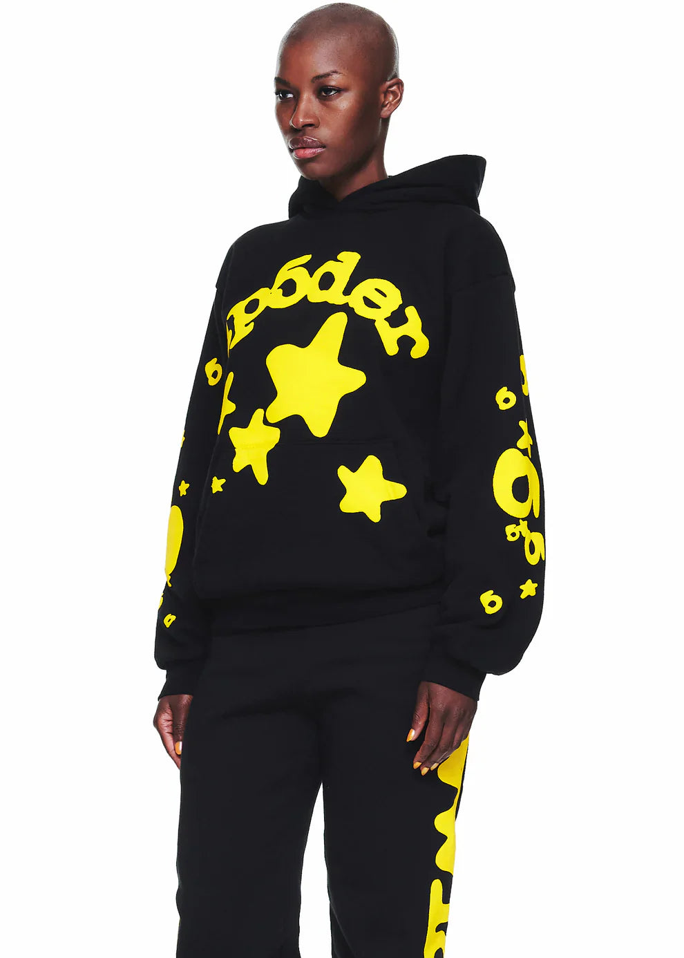 A person wears the Black Graphic Hoodie with Star Lettering Print— a comfort fit pullover featuring bold yellow star graphics and “Poder”—paired with matching pants, standing against a white background.