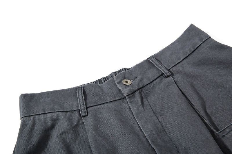 Close-up of dark gray pant waist with button closure and front pleats