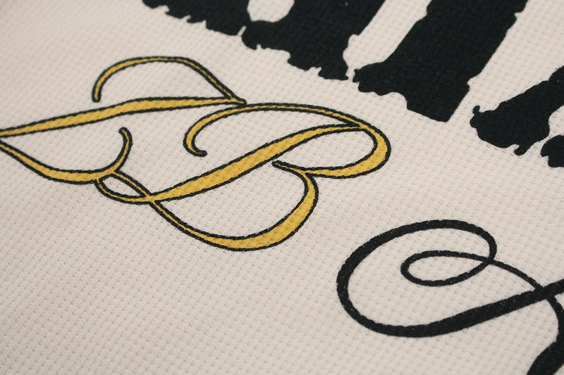 Close-up of gold BB lettering and black script on cream waffle knit fabric