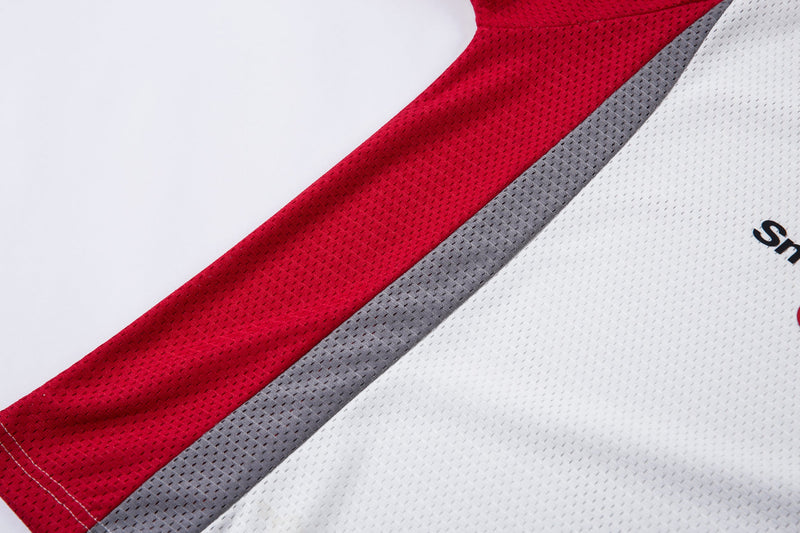 Close-up of a white mesh polo jersey with bold red and gray diagonal patchwork panels and partial logo detail