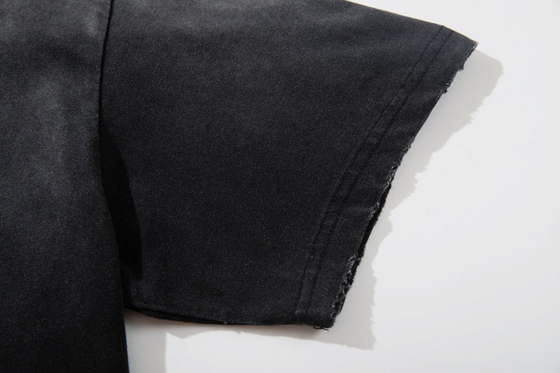 Close-up of a washed black grunge graphic tee sleeve with raw frayed hem and vintage distressed texture