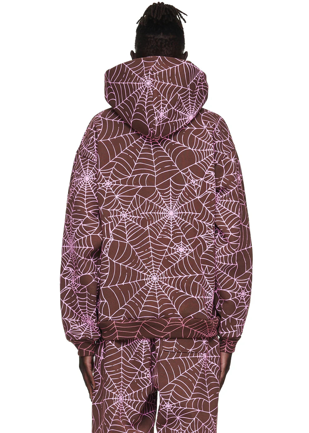 A person wearing the Brown All-Over Spider Web Graphic Hoodie – Comfort Fit Pullover Hoodie and matching pants, both featuring a pink spiderweb pattern on a brown background, is shown from the back.