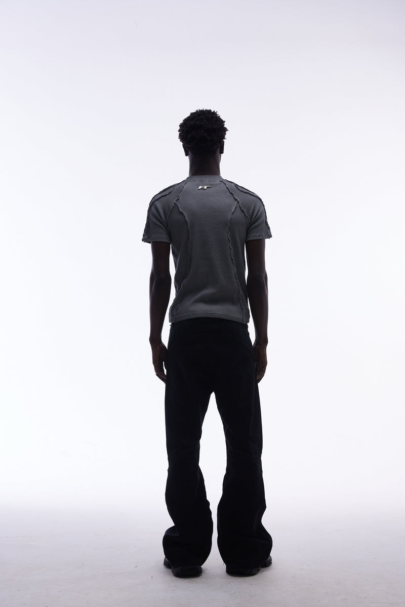 Model wearing a gray raw seam compression tee with deconstructed stitching, shown from the back with black pants against a white background