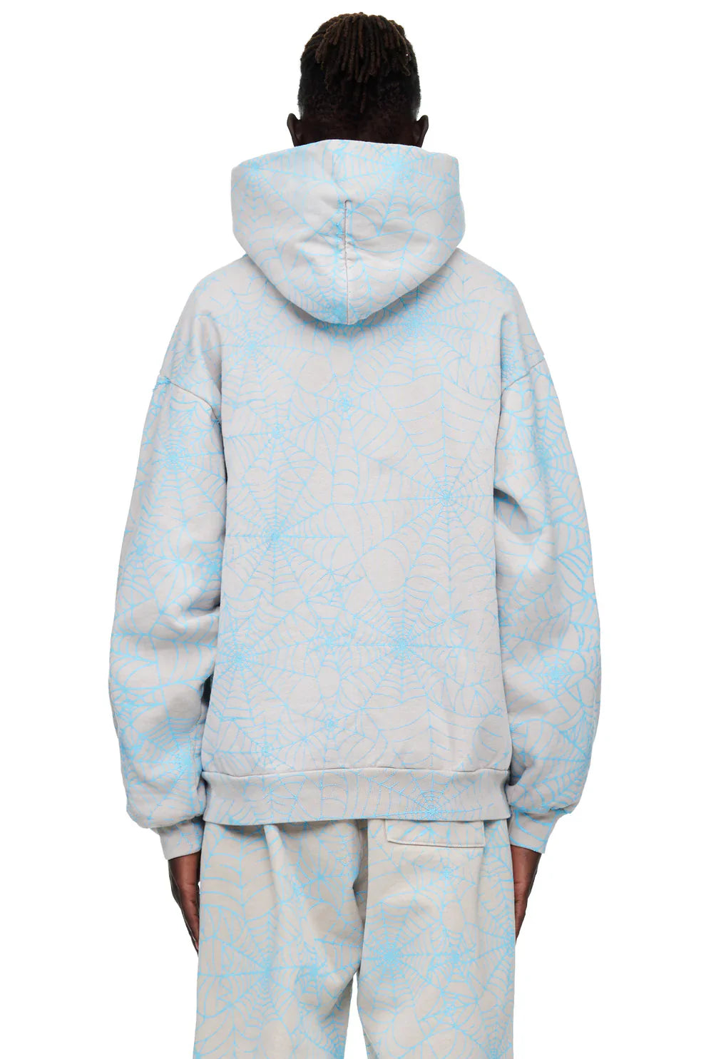 A person faces away from the camera wearing the hood up on a Light Grey All-Over Spider Web Graphic Hoodie – Comfort Fit Pullover Hoodie with matching pants in a pale blue web-like pattern.