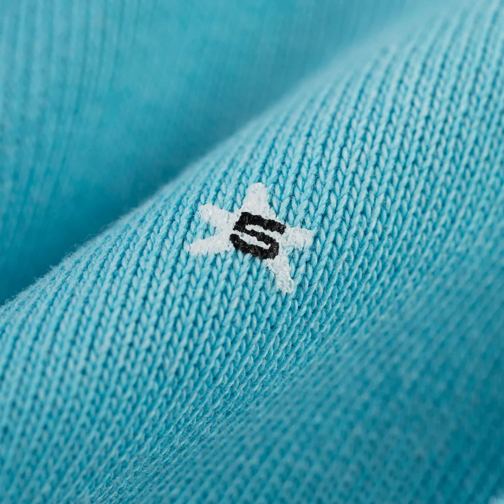 Close-up of the Turquoise Graphic Hoodie with Star Detail, showing a small white star with a black "S" embroidered at the center, capturing its comfort fit and signature style.