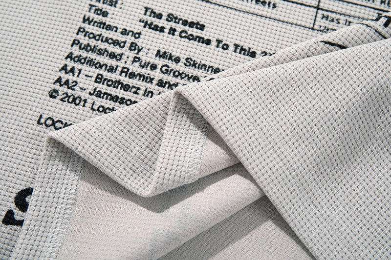 Close-up of a beige graphic T-shirt with black punk-style editorial text print and folded textured fabric details