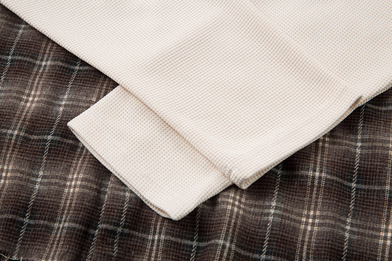 Layered sleeve detail with cream waffle-knit sleeve under brown plaid cuff