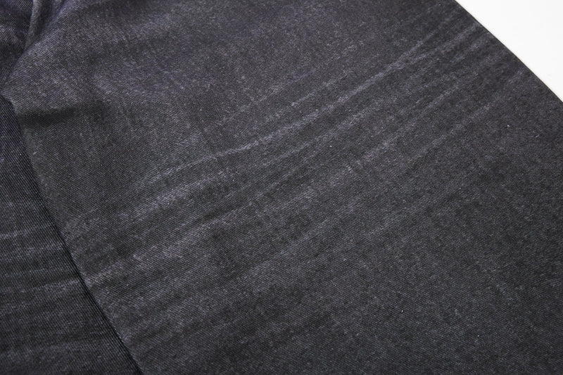 Close-up of black denim leg with subtle whiskering and faded distressing
