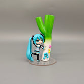 The Chibi Hatsune Miku Holding Green Onion 12cm PVC Figure playfully depicts the blue-haired character with headphones beside a large leek. Featuring a music note and star base, it embodies Hatsune Miku&