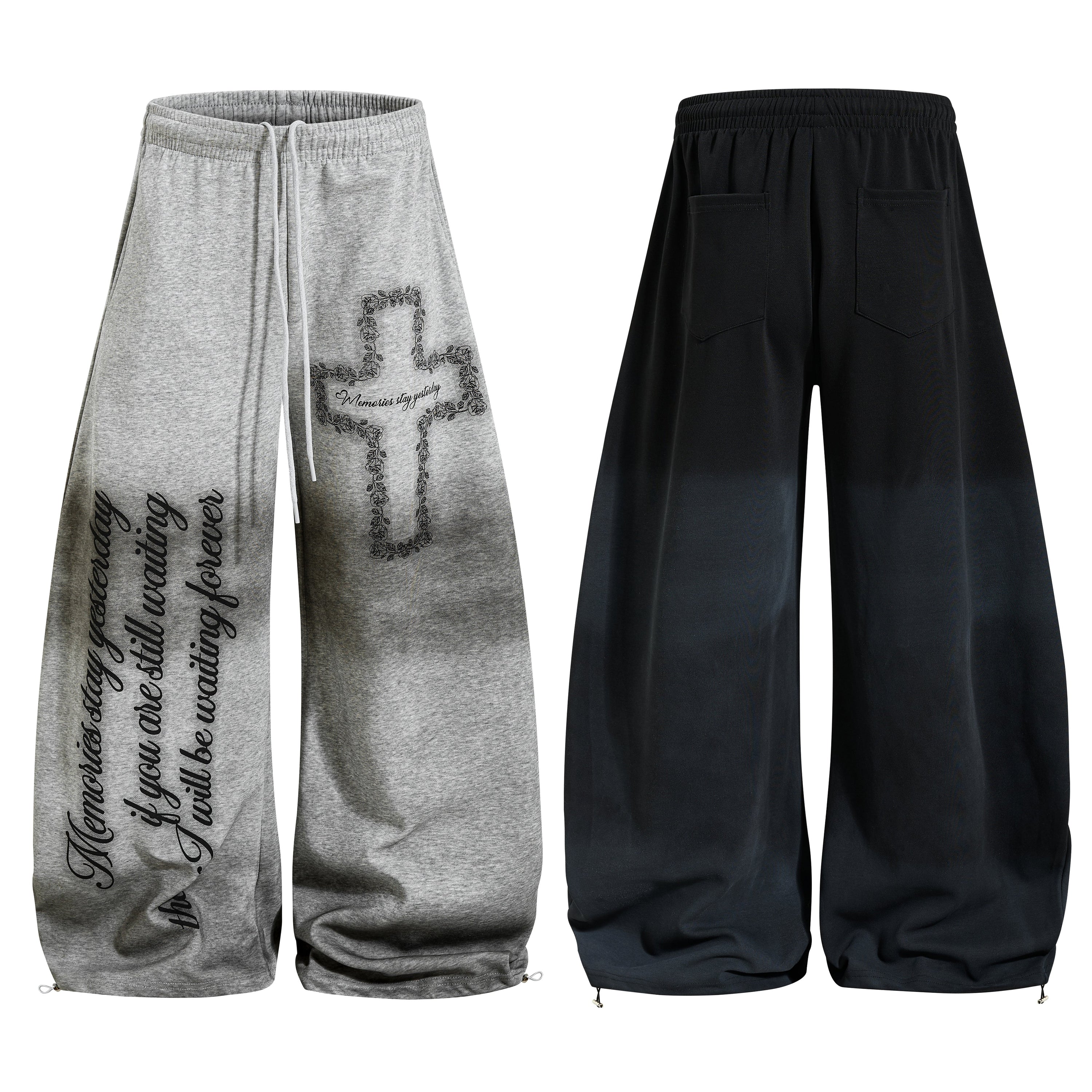Grey wide-leg sweatpants with floral cross graphic and gothic cursive script print on legs, shown front and back