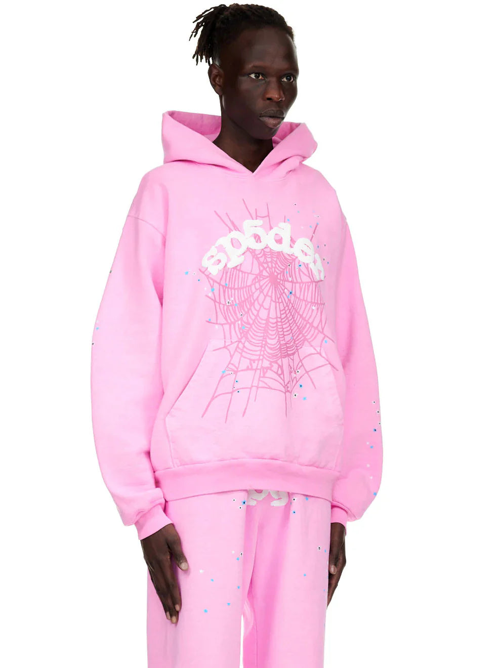 A person stands against a plain white background wearing the Pink Graphic Hoodie with Spider Web Print – a comfort fit pullover featuring a white spider web and sp5der logo, paired with matching pants.