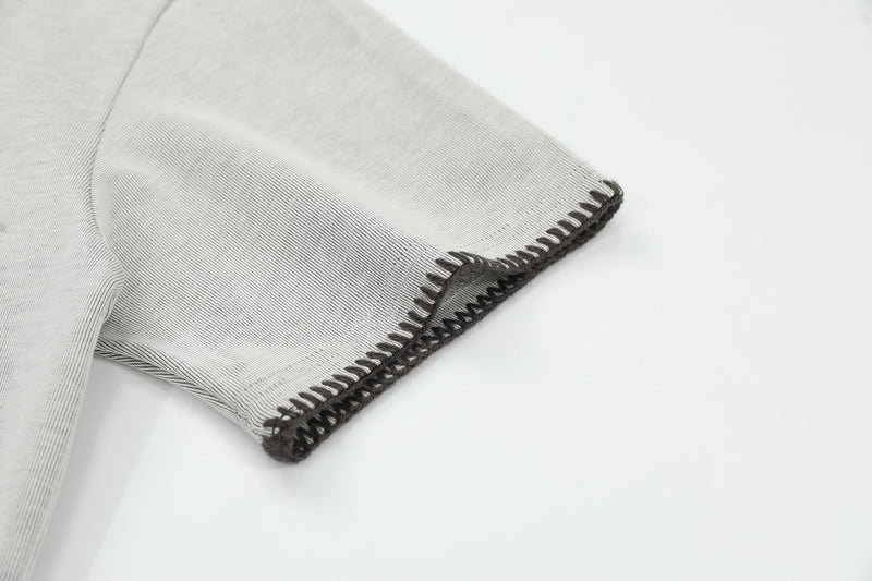 Close-up of light gray Henley tee sleeve with dark contrast stitching and raw hem detail on a clean white background
