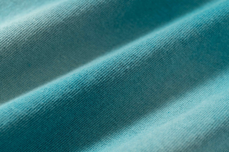 Close-up of teal washed cotton fabric with soft folds and textured knit, highlighting the vintage streetwear tee material