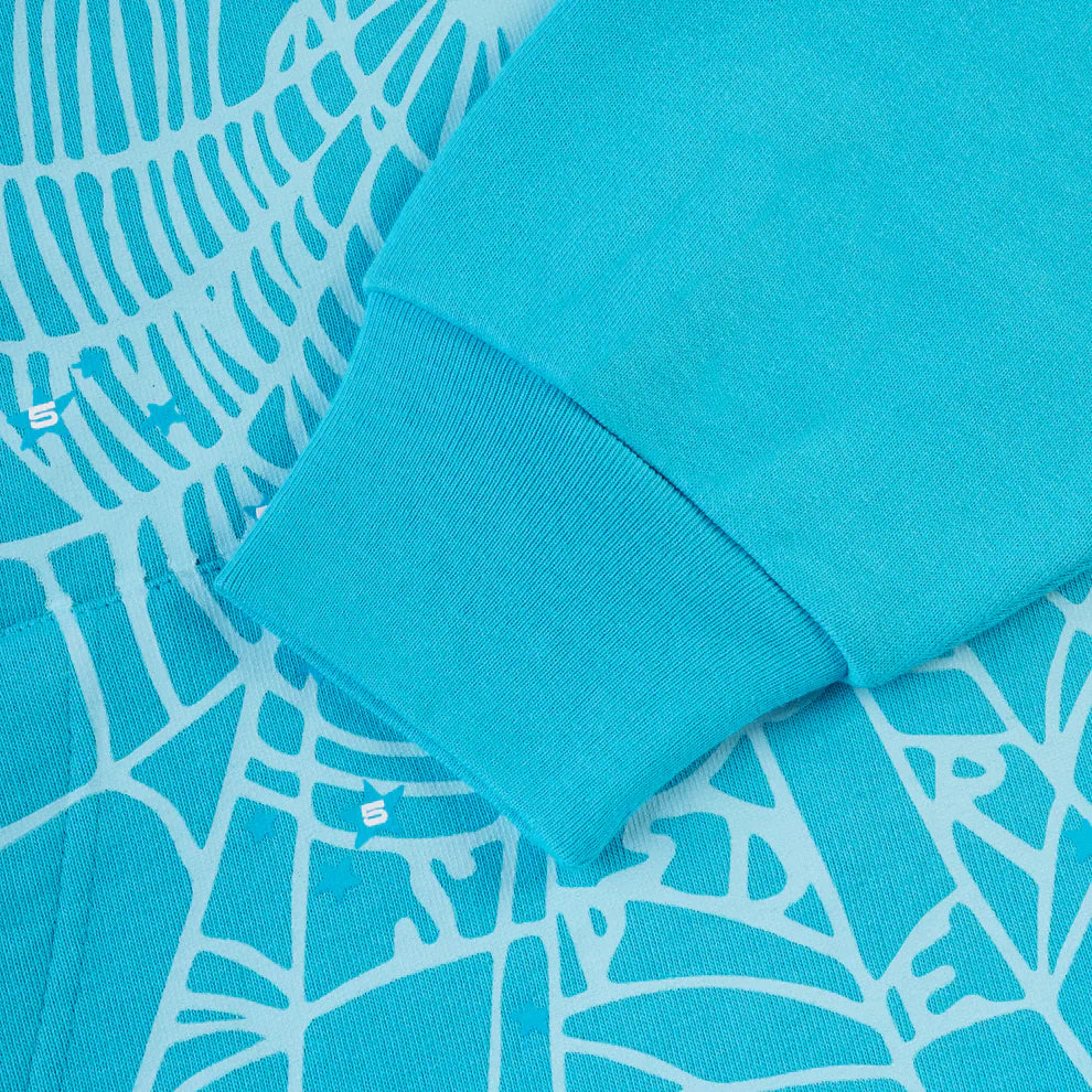 A close-up of the Sp5der “Nevermind the Spider” Hoodie in Sky Blue (440GSM heavyweight cotton fleece), showcasing its sleeve on fabric with an abstract white line pattern and small white S letters integrated into the design.