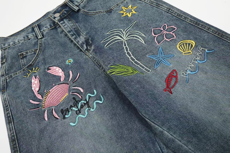 Close-up of front and side panels showing tropical embroidery on blue wide-leg jeans