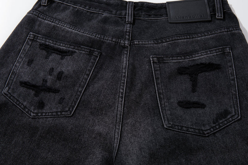 Close-up of back pockets on deep charcoal jeans with distressed patch details