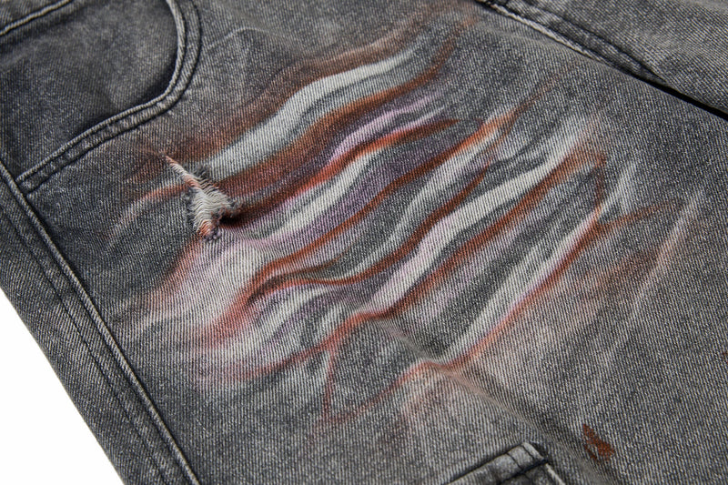 Close-up of gray jeans with pink, white, and brown paint streaks and a small tear