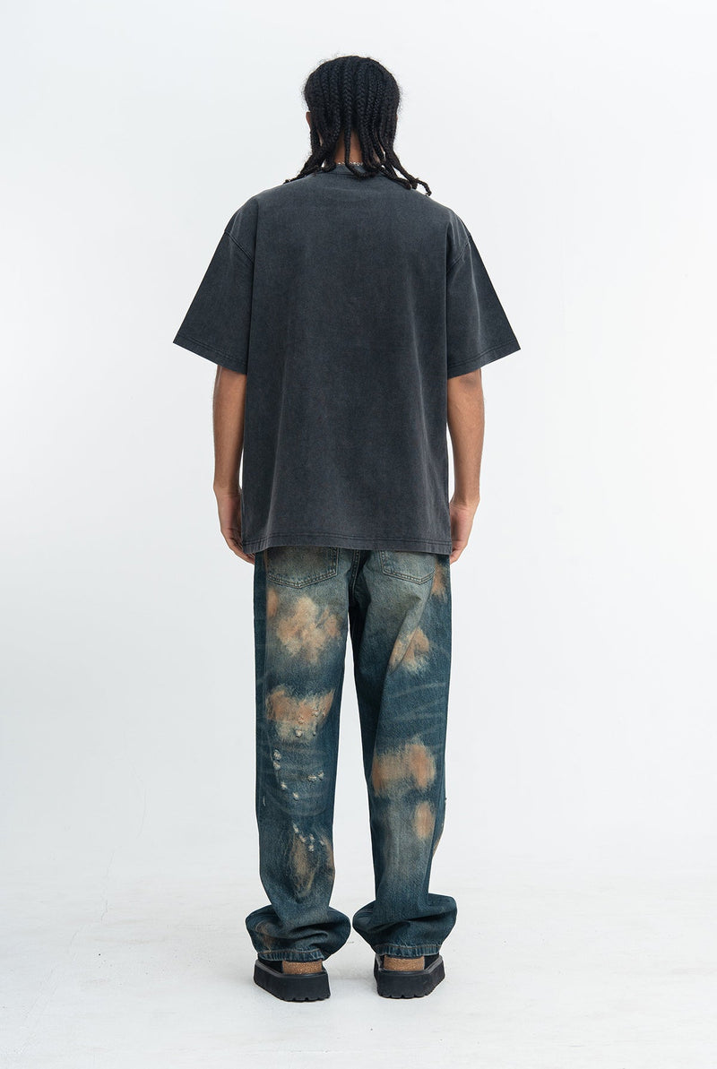 Back view of a model wearing a faded black vintage wash graphic T-shirt with baggy distressed jeans