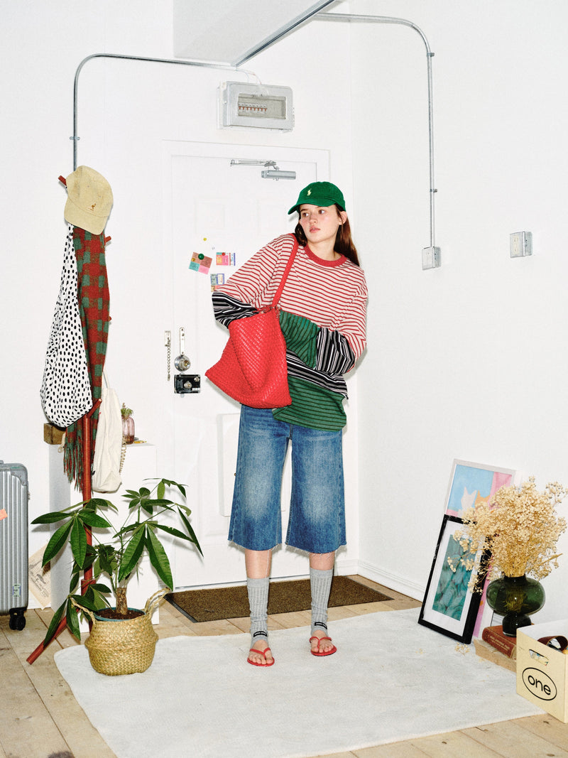 Model in color-block striped long sleeve tee, three-quarter view with red bag