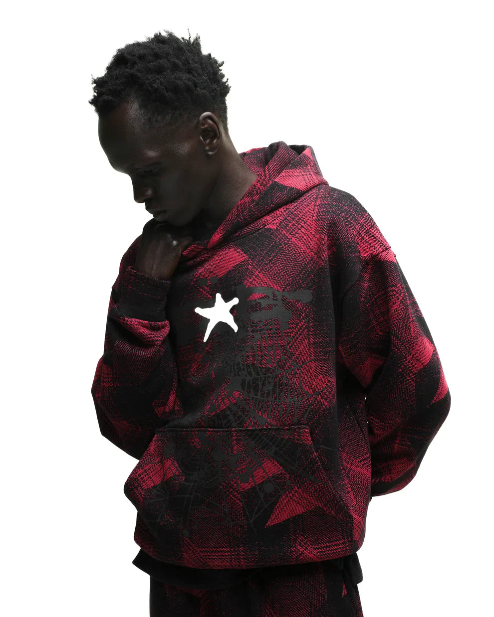 A person in the Red and Black Graphic Hoodie with Star Detail and Spider Web Print – Comfort Fit Pullover Hoodie stands against a white background, looking down thoughtfully with one hand near their chin.