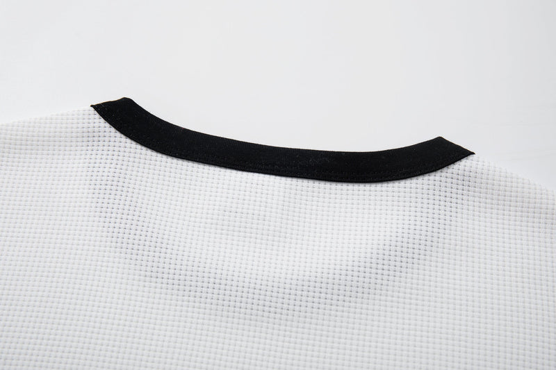 Close-up of a white waffle-knit graphic tee with a black ribbed crew neckline and textured fabric detail