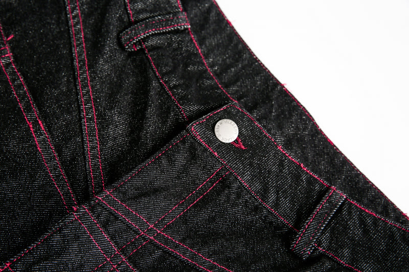 Close-up of black denim waistband and front button with red topstitching