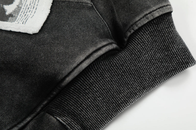 Close-up of black hoodie sleeve and ribbed cuff with part of a graphic patch