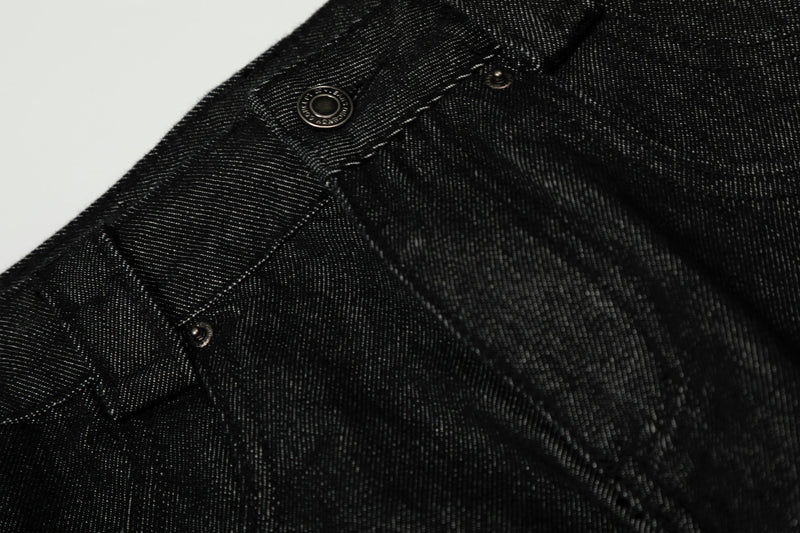 Close-up of black denim front waistband and pocket seam with metal button and topstitching
