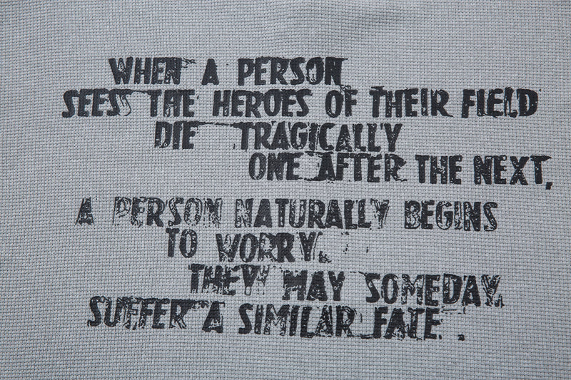 Close-up of a gray graphic tee with distressed black quote print and textured fabric background