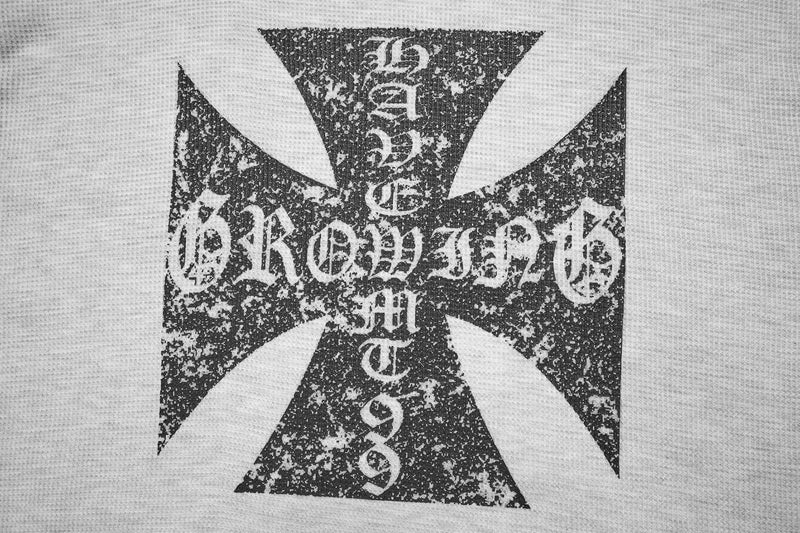 Close-up of distressed gothic cross logo on white waffle-knit sweatshirt