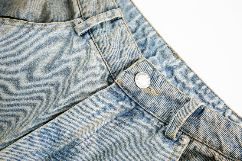 Close-up of denim waistband detail with metal button and belt loop on light wash jeans