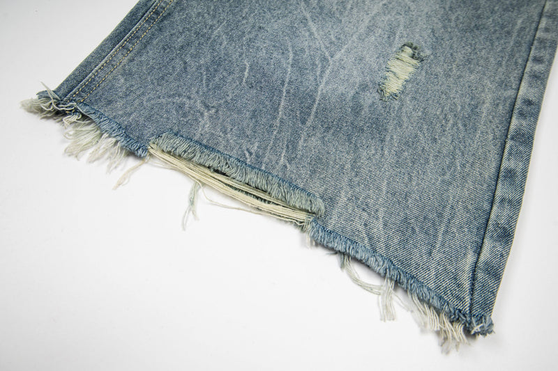 Close-up of frayed denim hem with distressed edge and small ripped patch