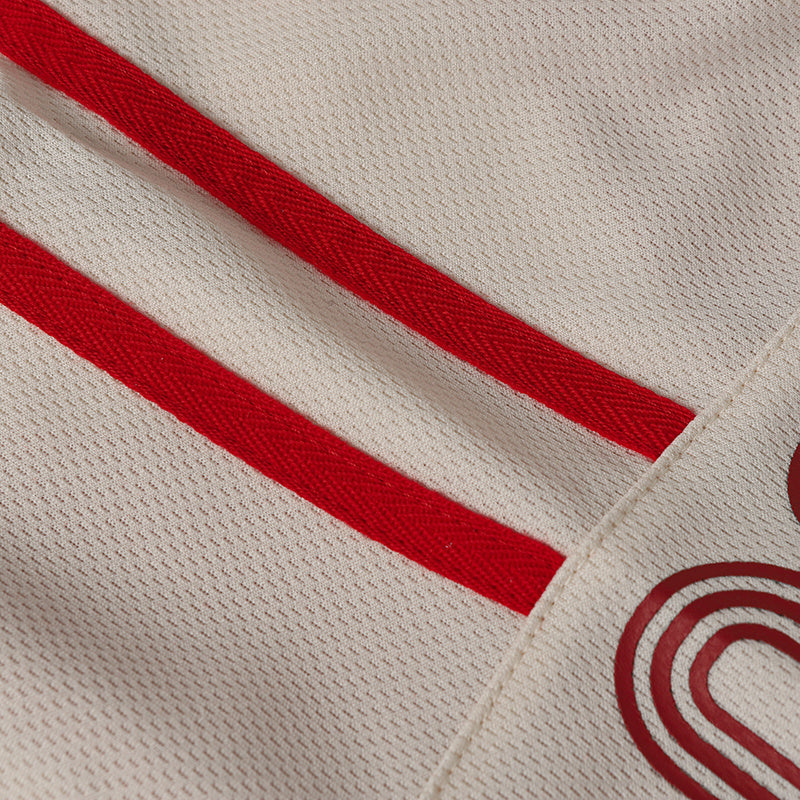 Close-up of a cream performance soccer jersey with red diagonal stripes and textured mesh fabric