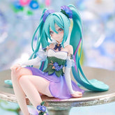 The Hatsune Miku Fairy 13.5cm PVC Figure, featuring long teal twin-tails and a fairy-inspired design, showcases the character in a purple and white floral dress. The figure is seated on a metallic surface against a blurred, colorful background, making it ideal for display.