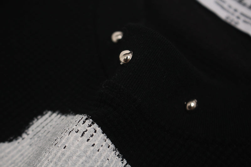 Close-up of black oversized graphic tee with metallic studs and distressed white cross print on fabric