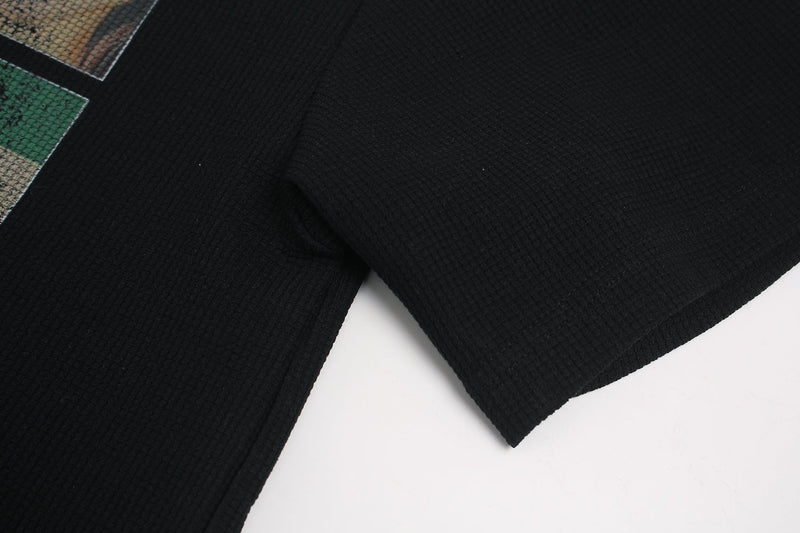 Black streetwear tee with ribbed texture and partial collage graphic print on the sleeve, close-up view