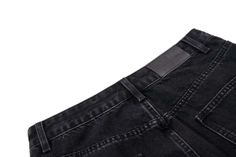 Close-up of black denim waistband with brand patch and belt loops