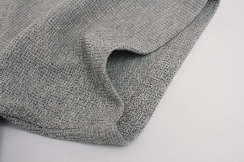 Close-up of gray waffle-knit fabric with folded hem, showing the textured material of a gothic streetwear graphic tee