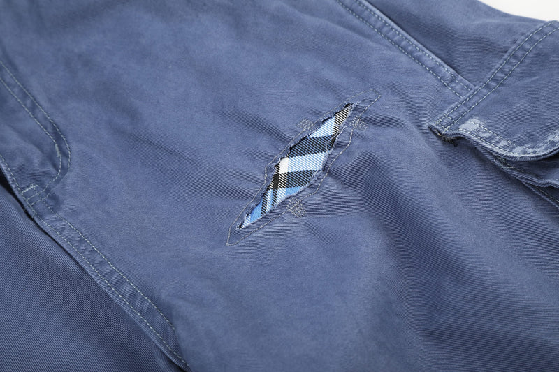Close-up of blue cargo shorts ripped hole with plaid lining and flap pocket
