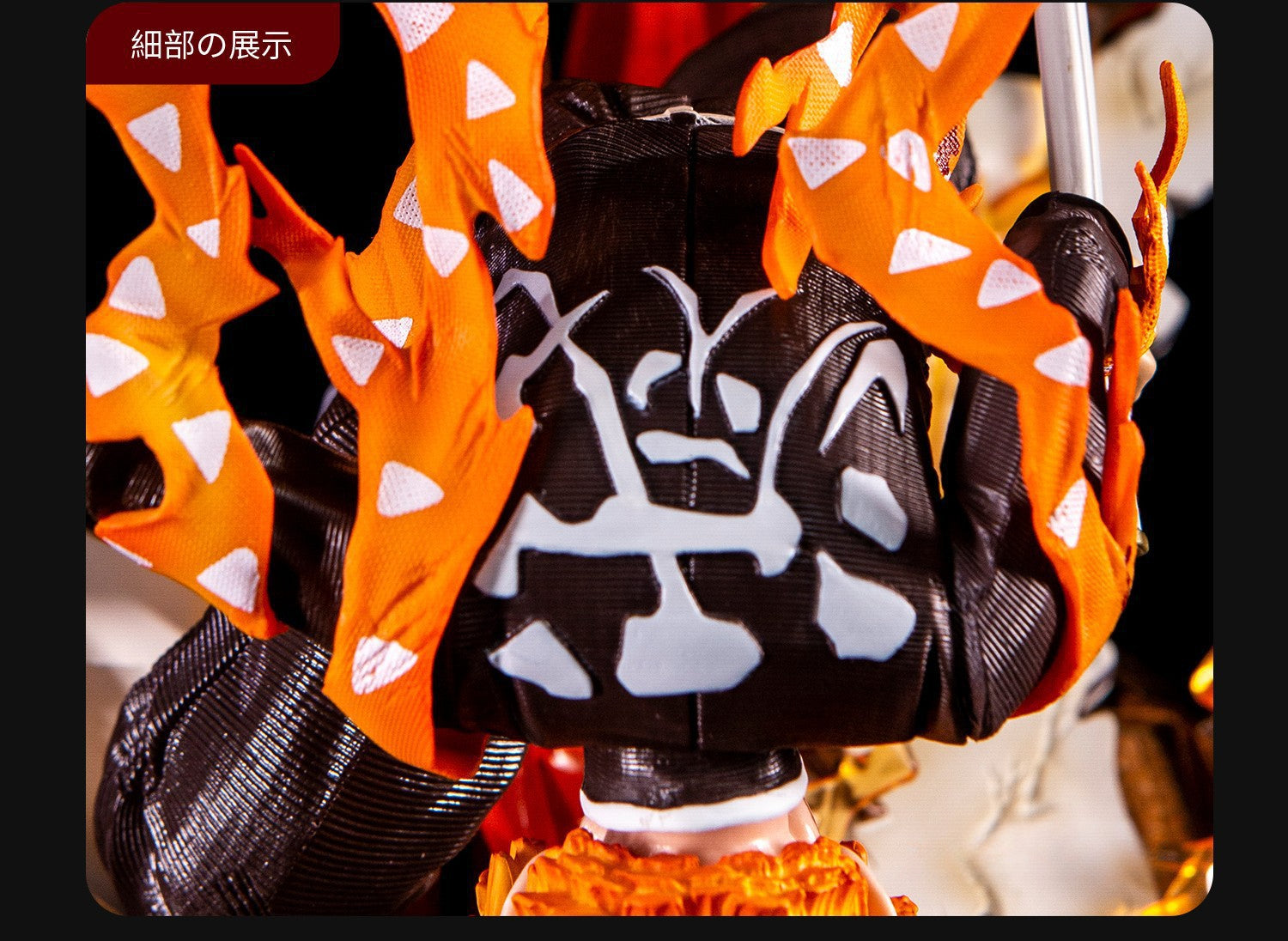 A close-up of the 28cm Rengoku Kyojuro Figure from Demon Slayer, depicting the Flame Hashira in a black cloak with white patterns and orange flame-like spikes featuring white triangles. The dark background enhances this high-quality PVC figure&