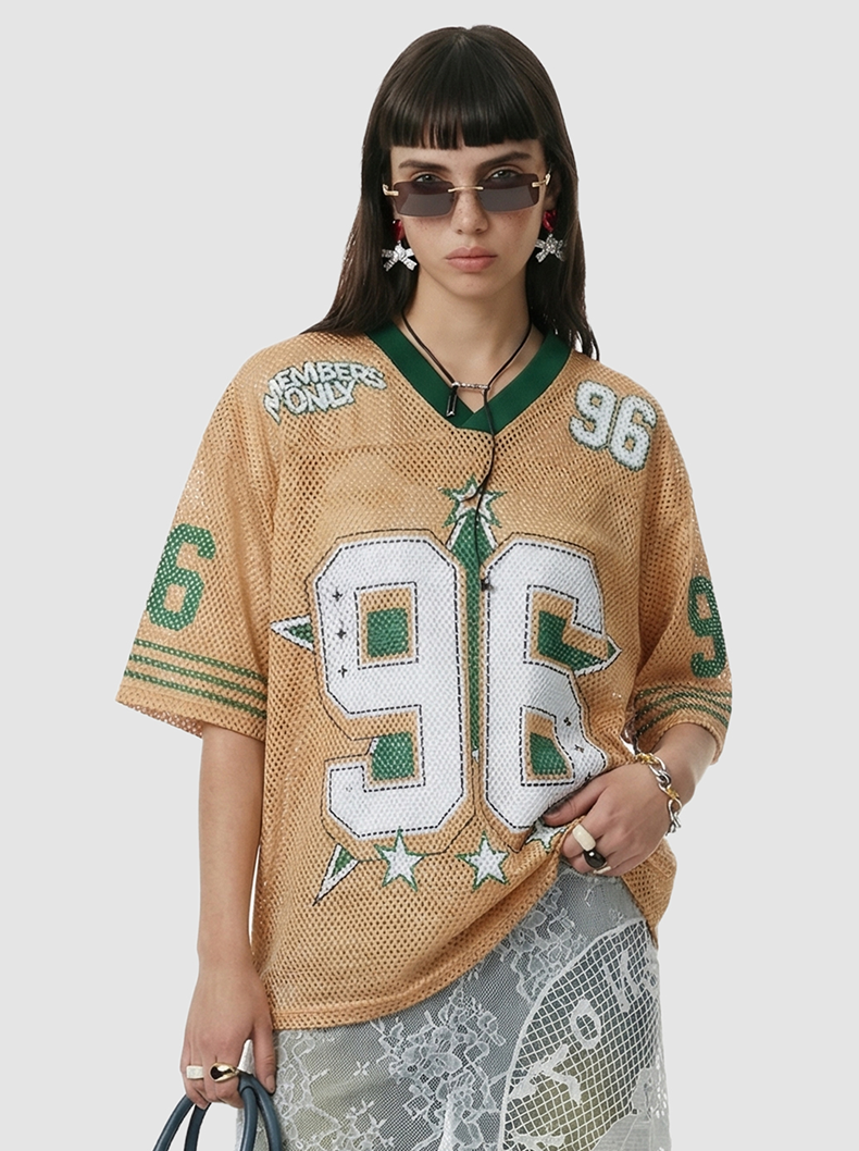 Model wearing a tan mesh streetwear jersey with green trim and large 96 graphic, styled with sunglasses and jewelry