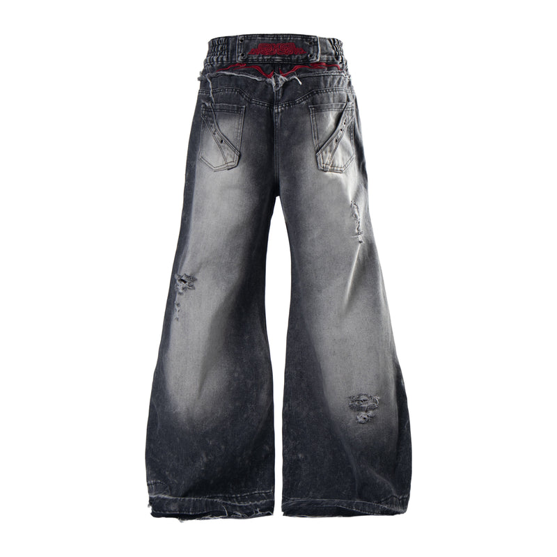 Back view of faded black baggy jeans with wide legs, distressed details, and embroidered back waistband