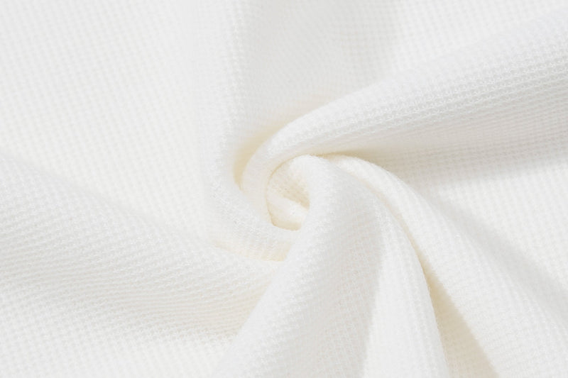 Close-up of soft white fabric with a textured knit surface and folded drape, showing the shirt material detail